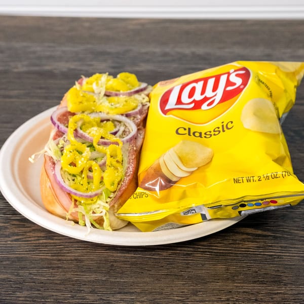A Rosie's Corner Take Out sub sandwich with red onions and peppers, served with a bag of Lay's chips.