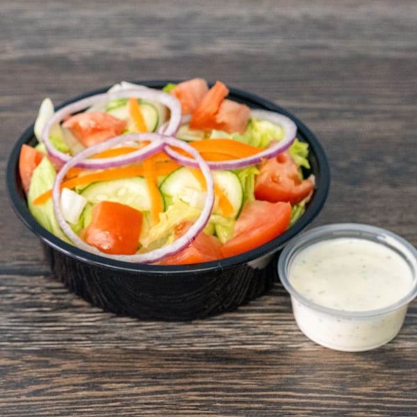 Fresh garden salad with lettuce, tomatoes, cucumbers, carrots, and red onions, with a side of dressing.