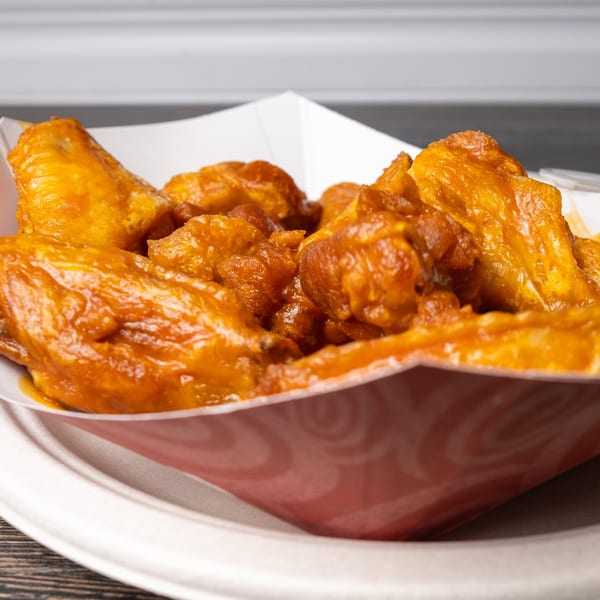 Rosie's Corner Take Out Restaurant's buffalo wings, coated in a glistening orange sauce, served in a paper tray.
