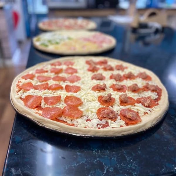 Three uncooked pizzas with various toppings, including pepperoni and sausage, on a dark countertop.