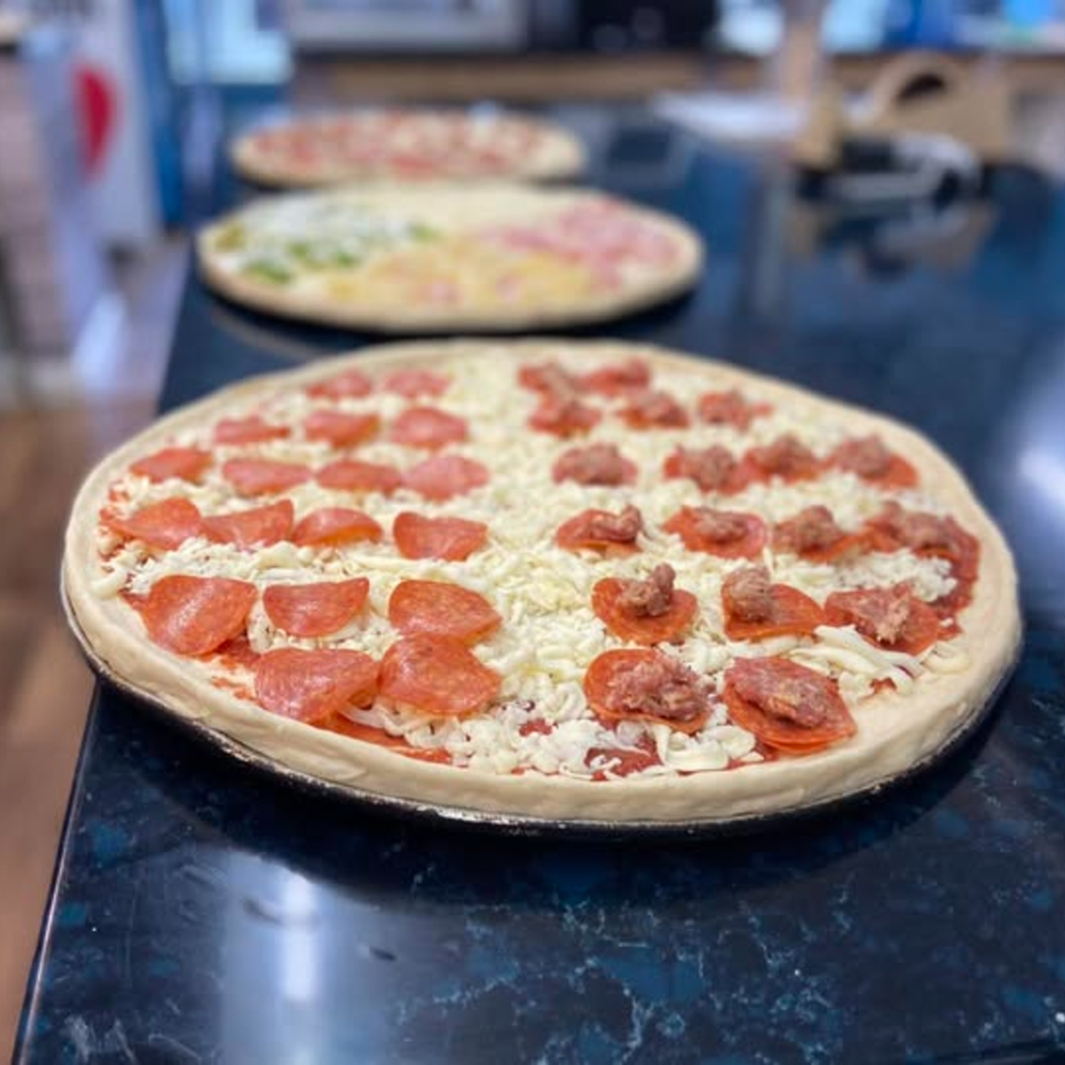 Three uncooked pizzas with various toppings, including pepperoni and sausage, on a dark countertop.